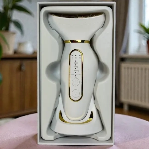 Urządzenie do pielęgnacji twarzy z funkcjami EMS i terapią LED zapakowane w eleganckie pudełko, biało-złoty design, widok frontalny, stylowe wnętrze w tle.