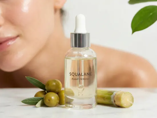 Szklana butelka skwalanu pochodzenia roślinnego na marmurze, obok zielonych oliwek i trzciny cukrowej, z rozmyciem kobiety i laboratorium w tle.